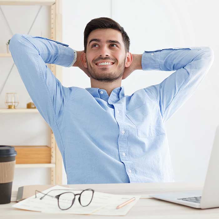 Young positive office man having rest in office, spreading elbows, stretching his back, taking break from work tasks and projects, smiling happily, looking to left