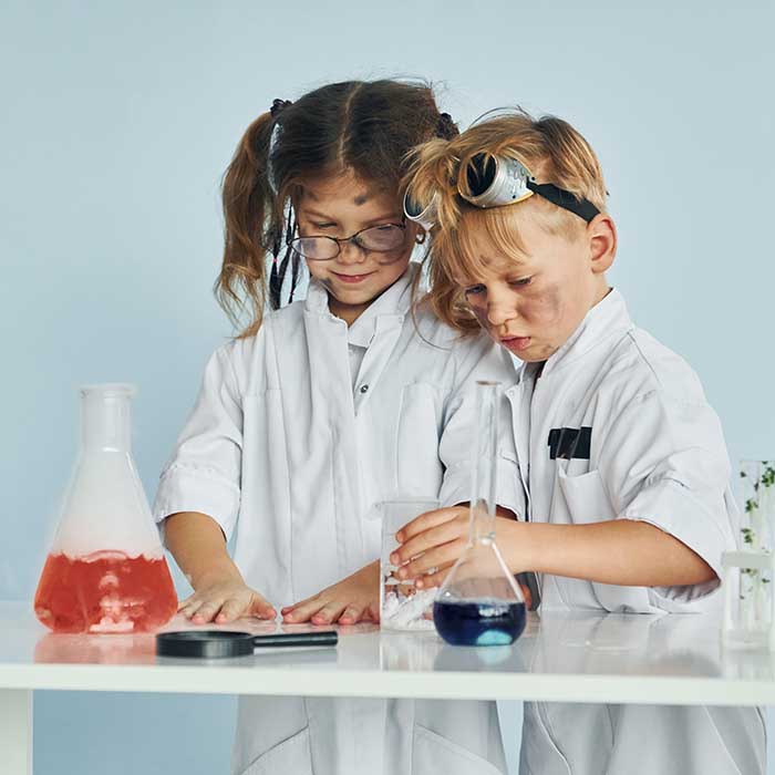 Little girl and boy in white coats plays a scientists in lab by