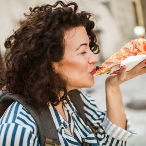 Beautiful young curly hair woman eating a slice of pizza outdoor