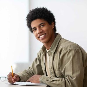 Portrait of positive black teenage student with laptop and noteb